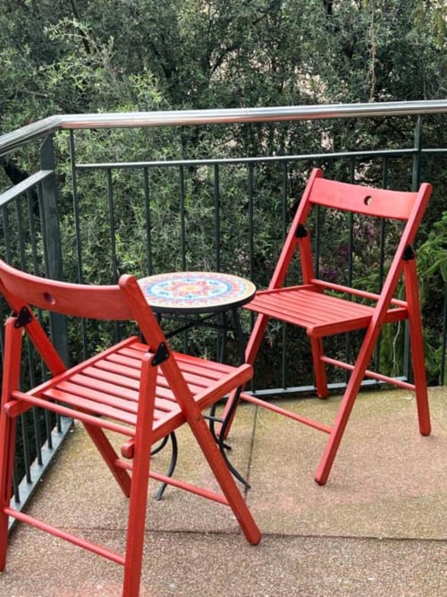 Sillas rojas plegables con mesa decorativa en la terraza de los apartamentos Tessa, Matadepera, con vistas al exuberante jardín