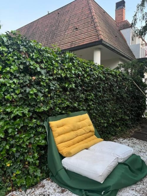 Silla de descanso acolchada verde y amarilla en el área de jardín privado de los apartamentos Tessa, Matadepera, rodeada de setos exuberantes