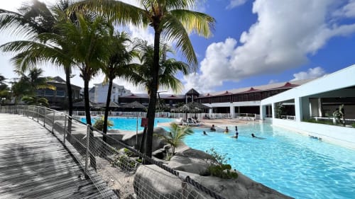 Caribluewave Appartements pool area in St-François with palm trees, turquoise water, and guests swimming