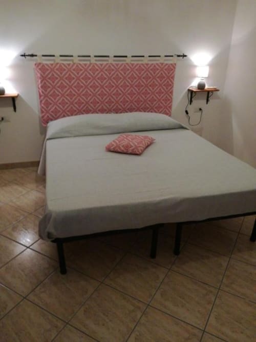 Camera da letto di Zia Amalia Villa Asfodelo ad Alghero con testata rosa decorata, biancheria bianca e lampade comodino