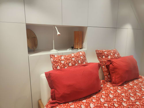 Studio cosy à La Conciergerie de Nathalie avec literie rouge à motifs, oreillers et étagères blanches modernes
