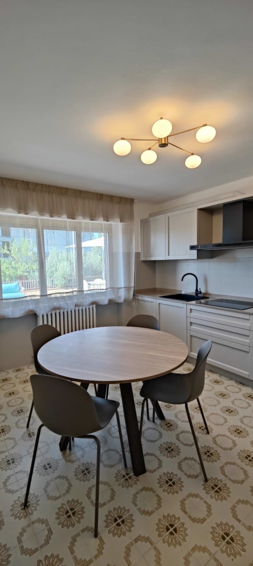 Moderna zona cucina-pranzo con tavolo rotondo, sedie nere, lampada in ottone e vista sul lago