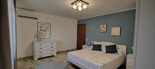 Camera da letto moderna con parete accent teal, arredamento bianco e vista sul lago presso Villa Italia Management