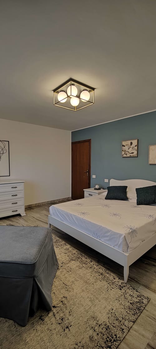Camera da letto moderna con lampada da soffitto esagonale, letto bianco, parete accent turchese, pavimenti in legno, TV e scrivania