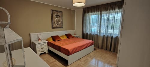 Camera moderna con biancheria arancione, mobili bianchi e vista sul lago dalla finestra con tende di Villa Italia