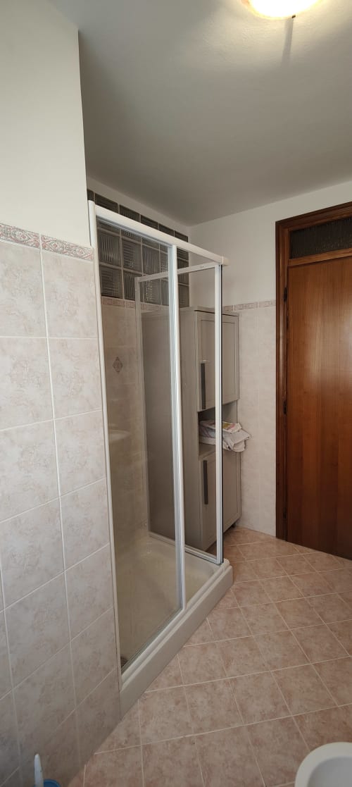 Bagno moderno con doccia aperta, piastrelle beige su pavimento e pareti, sanitari bianchi, porta in legno a Villa Italia