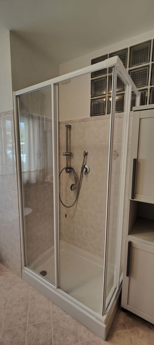 Moderna cabina doccia in vetro con telaio bianco e soffione manuale nel bagno accessibile dell'appartamento a Villa Italia