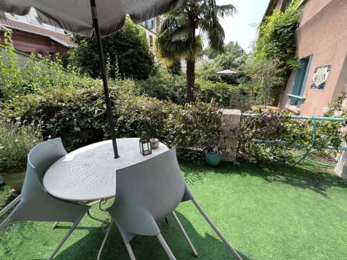 Terrasse ensoleillée de la Maison 1850 Paris avec table blanche moderne, chaises et parasol noir entourés de verdure luxuriante