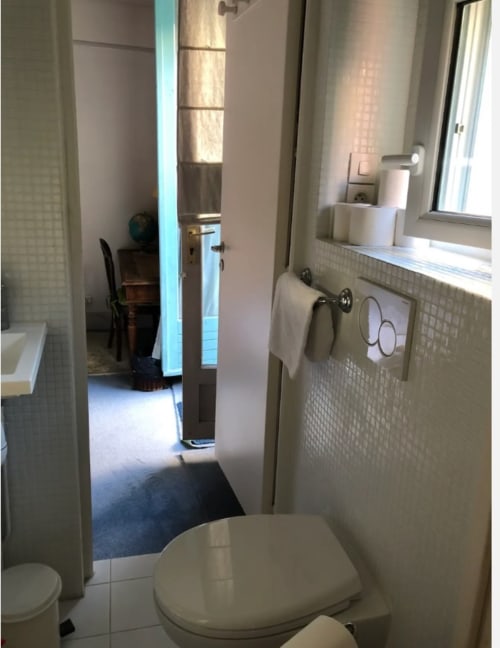 Salle de bain moderne dans la chambre de Gaspard à Maison 1850 Paris, avec carrelage blanc, toilettes, lavabo et vue sur le couloir