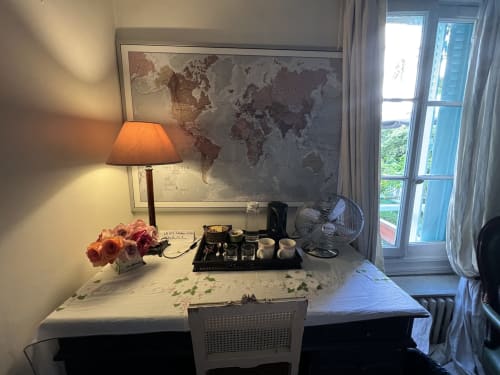 Bureau de la Chambre d'hôtes à Paris avec carte du monde, lampe de bureau, ventilateur et fleurs surplombant la terrasse-jardin de la Maison 1850