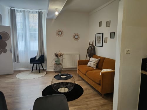 Salon moderne à Dinan avec canapé orange, décoration murale et vue sur la ville depuis les fenêtres