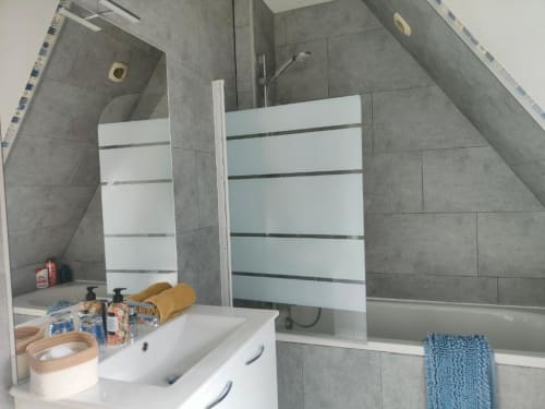 Salle de bain moderne à La Conciergerie de Nathalie à Dinan avec carrelage gris, lavabo blanc, baignoire et paroi de douche en verre teinté