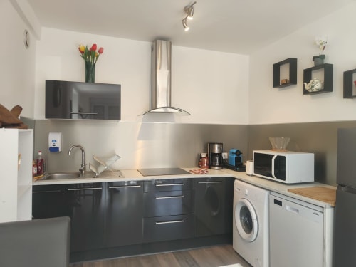 Cuisine moderne de l'appartement de Dinan avec armoires noires, électroménagers inoxydables, lave-linge et murs blancs