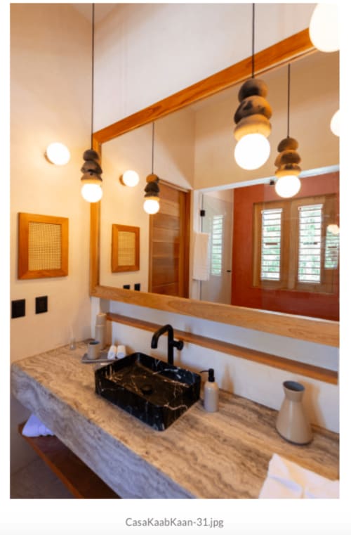 Baño moderno de la villa Kaab Kaan House en Tulum, con lavamanos de mármol negro, tocador de madera, lámparas colgantes y espejo grande