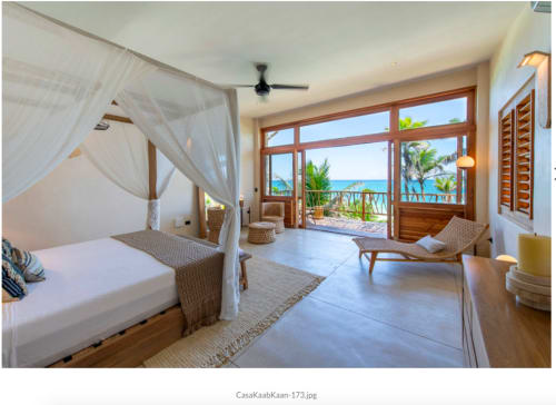 Lujosa habitación de villa frente al mar en Tulum con cama con dosel, balcón con vista al océano y comodidades modernas