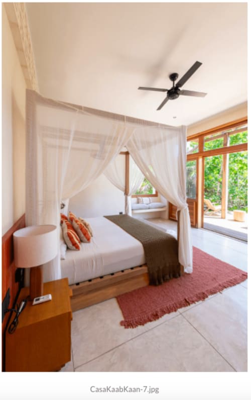 Cama con dosel lujoso y cortinas blancas translúcidas en villa Kaab Kaan House, Tulum, con ventilador de techo y vistas al océano