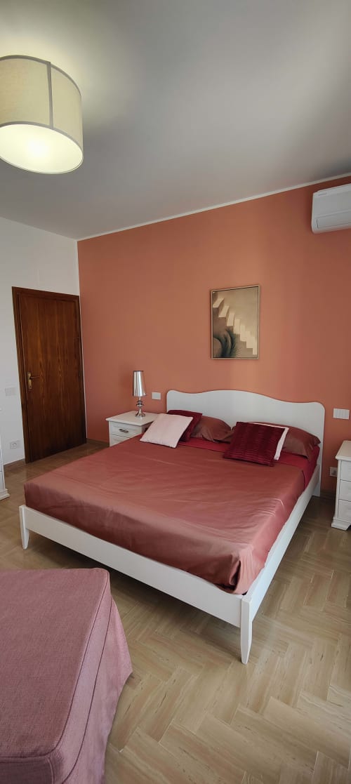 Modern bedroom with coral accent wall, white bed, and wooden flooring at Villa Italia Management apartment