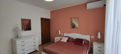Modern bedroom with coral accent wall, white furniture, and burgundy bedding at Villa Italia apartment