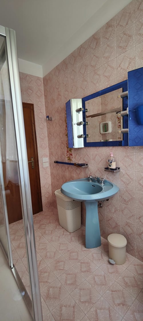 Modern bathroom with blue pedestal sink, mirror cabinet, pink tiled walls, shower, and amenities at Villa Italia apartment