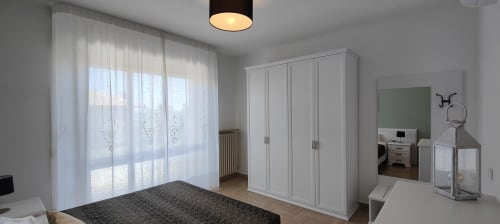 Modern apartment bedroom with lake view, white wardrobe, sheer curtains, and contemporary furnishings at Villa Italia