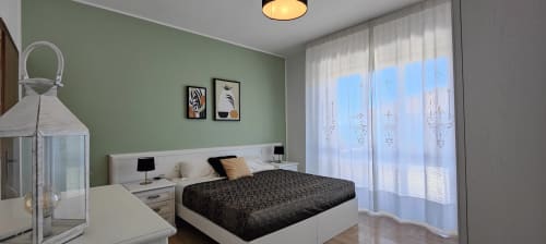 Modern bedroom with sage green walls, white bed, black bedding, and lake view through sheer curtains at Villa Italia