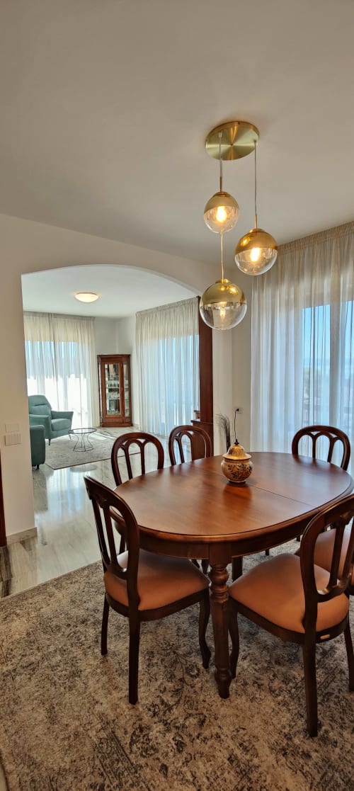 Modern dining room with wooden table, brass pendant lights, and lake views through floor-to-ceiling curtains