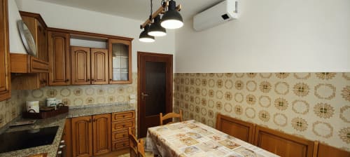 Spacious kitchen and dining room in Italian apartment with wooden cabinets, patterned wallpaper, and dining table.