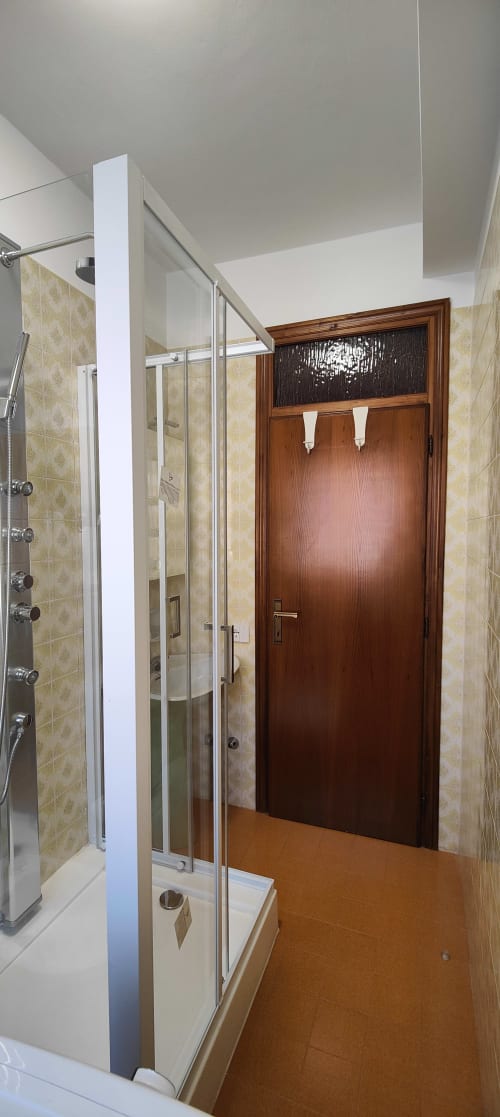 Modern bathroom with glass shower enclosure, beige patterned tiles, and wooden door at Villa Italia Management apartment