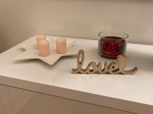 Arredo accogliente all'appartamento GioviGemini con insegna 'love' in legno, candele rosa e candela profumata ai frutti di bosco su scaffale bianco