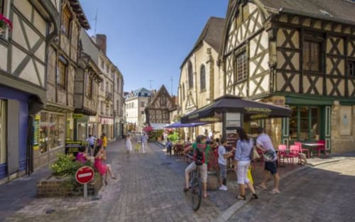 Des bâtiments à colombages médiévaux bordent une charmante rue piétonne à Domérat, avec terrasses de café et boutiques.