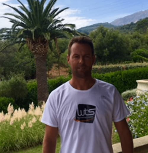 Homme en chemise WTS blanche au jardin de La Conciergerie du Cap Corse à Centuri avec palmier et montagnes