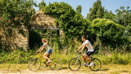 Deux cyclistes passent devant des ruines de pierre recouvertes de lierre près du Gîte du Miroir à Domérat, en France