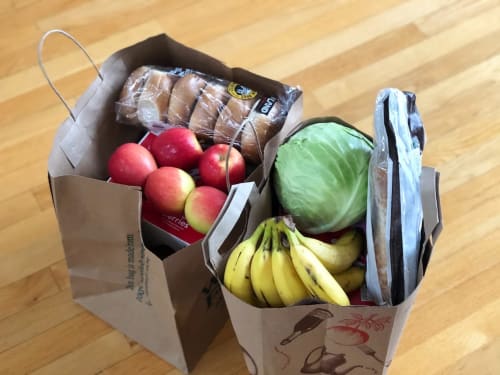 Grocery delivery bags with fresh produce, bananas, cabbage, apples, and packaged items on wooden floor, Tulum hotel service