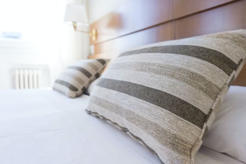 Almohadas de lino a rayas en cama de habitación de hotel en Tulum con lámpara de noche y radiador visible