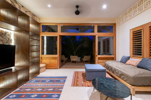 Sala de estar de villa moderna en Tulum con muebles de madera, puertas con vistas al mar, alfombras azules con patrón y asientos cómodos