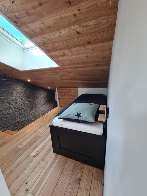 Chambre moderne à CMD Méribel Le Pralin avec plafond en bois, puits de lumière, lit noir et coussin étoilé bleu, mur de briques sombres