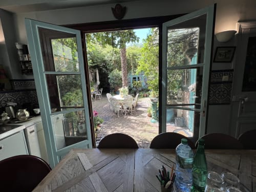 Salle à manger de la villa parisienne avec vue sur le jardin par les portes turquoise, table en bois et accès à la terrasse à la Maison 1850