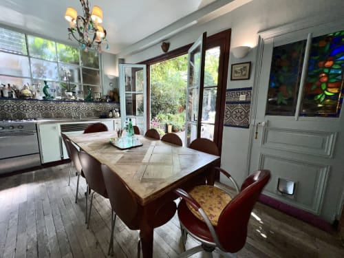 Élégante salle à manger de villa parisienne avec vue sur jardin, table en chevron, chaises bordeaux et lustre orné