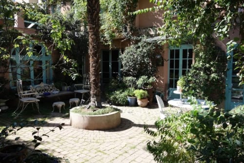 Cour luxuriante de la Maison 1850 Paris avec murs de lierre, patio en brique, plantes en pot et portes turquoise
