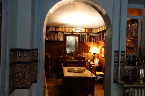 Élégante bibliothèque parisienne avec portail en arche, rayonnages en bois foncé, cheminée et mobilier d'époque à la Maison 1850