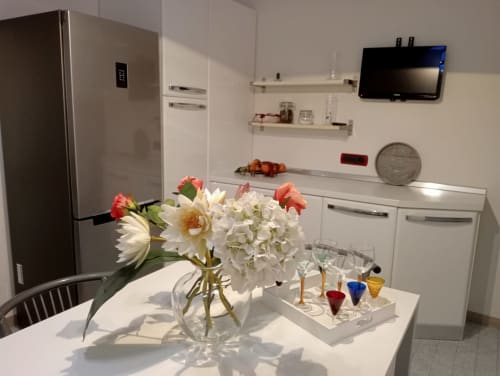 Cucina moderna dell'Apartment GioviGemini a Treviso con mobili bianchi, fiori sul tavolo da pranzo e TV a muro