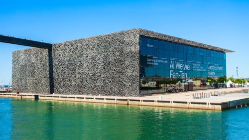 Bâtiment musée contemporain au bord de l'eau avec façade texturée du MuCEM à Marseille, eaux bleues et ciel dégagé