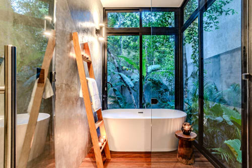 Baño moderno en villa de Tulum con bañera independiente, vistas al jardín, toallero de escalera de madera y exuberante vegetación tropical