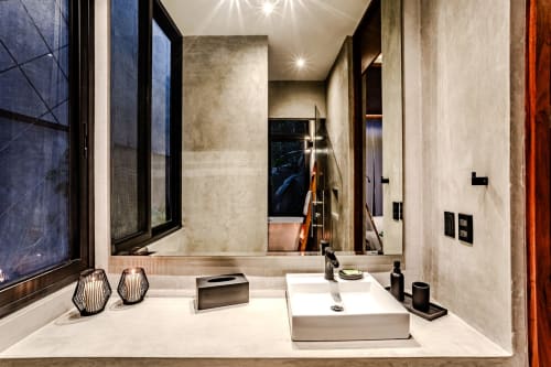 Baño moderno en villa de Tulum con lavamanos blanco, espejo grande, muros de concreto y accesorios negros