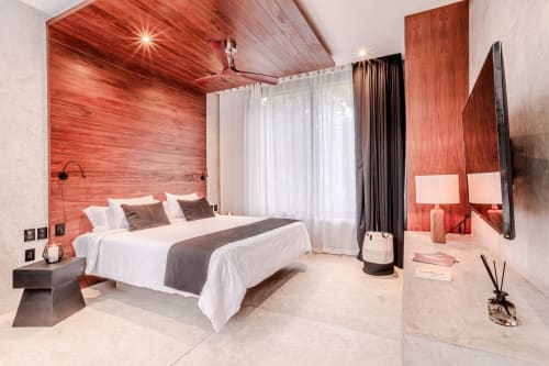 Lujosa habitación de villa Karmond House en Tulum con pared de acento en madera roja, ropa de cama blanca, TV de pantalla plana y vistas al jardín