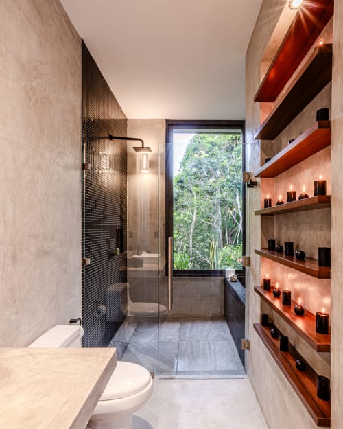 Baño moderno en villa Karmond House en Tulum con ducha de azulejos negros, repisas de madera con velas y ventana con vista al jardín