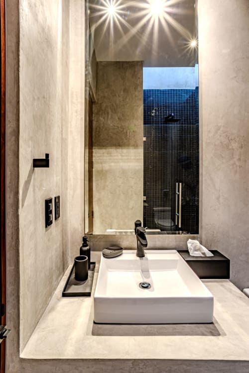 Moderno lavabo de baño con pileta elevada, herrajes negros y vista del espejo hacia la ducha en villa de Tulum