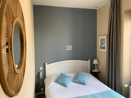 Single bedroom at Hôtel Maison Richet with white bed, blue accent pillows, slate blue accent wall, and decorative wooden