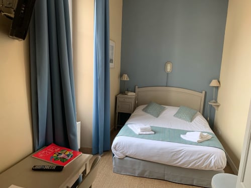 Cozy double bedroom at Hôtel Maison Richet in Les Sables-d'Olonne with cream bed, blue curtains, and modern amenities