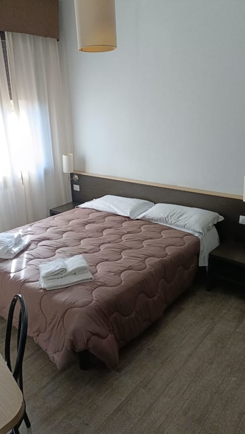 Camera da letto Hotel Eden a Vignola con letto trapuntato, cuscini bianchi, lampada a sospensione e tende trasparenti